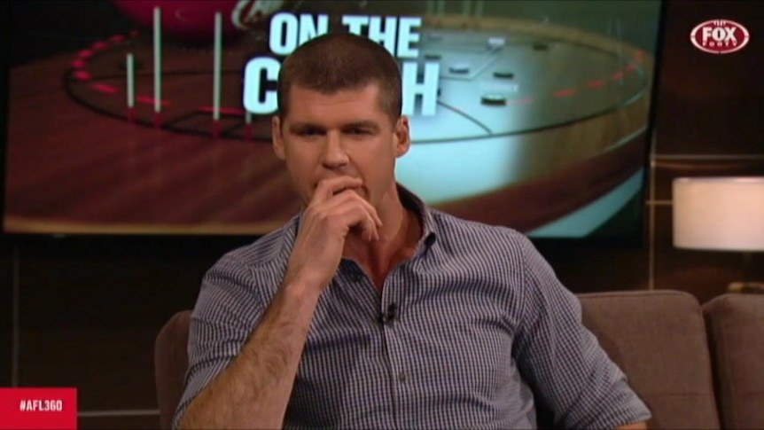 Jonathan Brown holds his hand up to his mouth as he sits on a couch presenting the AFL 360 TV show.