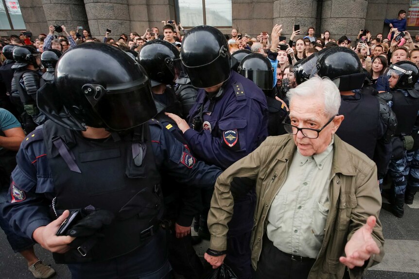 Police officers are seen detaining an elderly man during a rally.