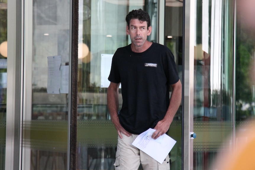 A man in a black T-shirt exists the front doors of the court building.