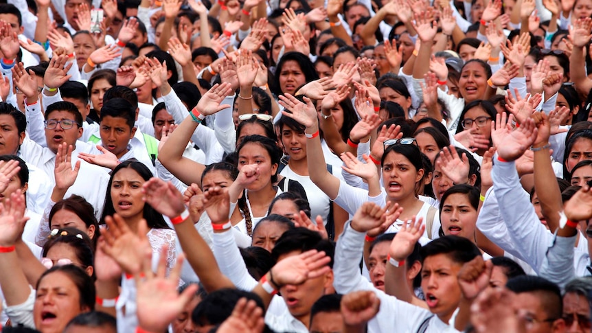 A crowd of people wave their hands while attending an open-air church rally.