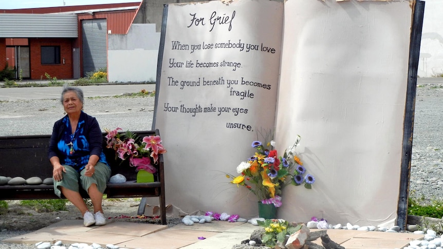 A woman sits next to a monument at site of the now-demolished CTV building in Christchurch.