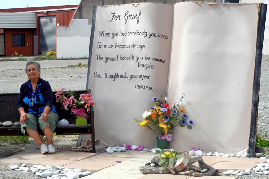 A woman sits next to a monument at the site of the now-demolished CTV building in Christchurch.