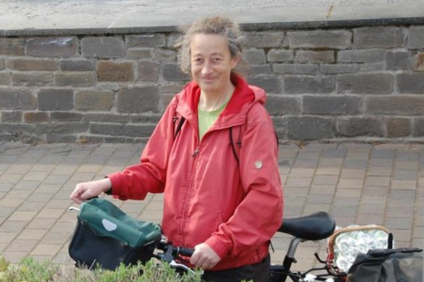 Ms Billen stands smiling in a red jacket holding a bicycle