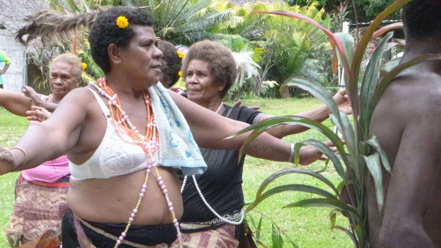 Women dancing in Vanuatu, with one wearing a bra with a flower in her hair.