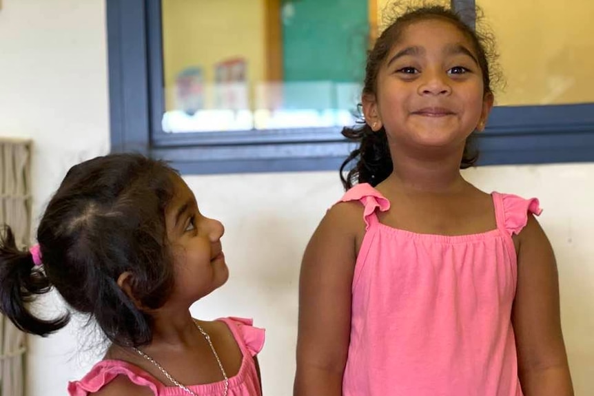 Two sisters wearing matching pink dresses smile