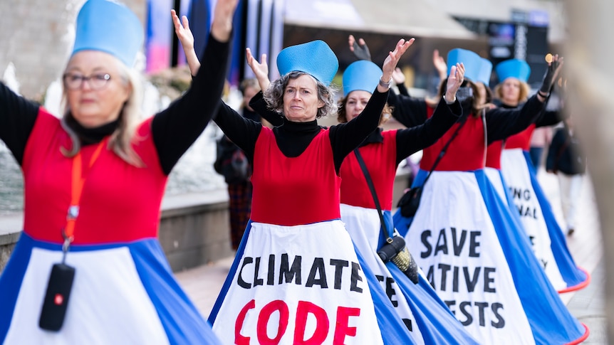 Five women stand in a line, they frown as they protest climate change