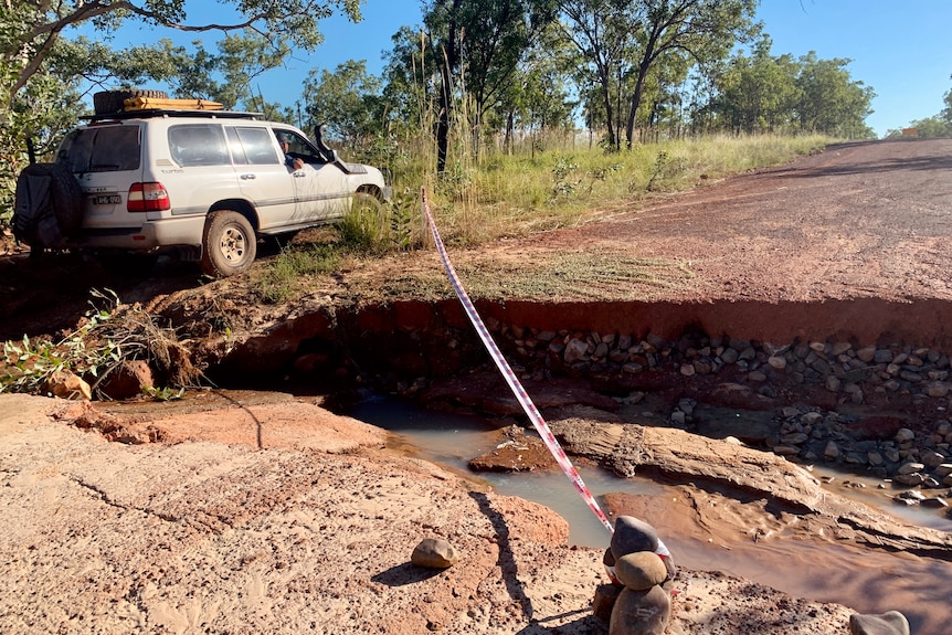 A white car parked next to a flood-damaged dirt track with warning tape marked around it.