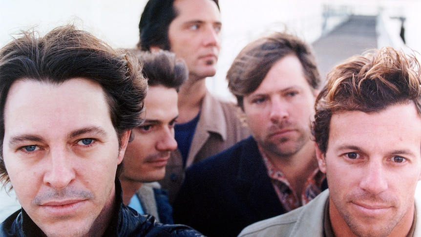 Powderfinger members stand close together all wearing jackets