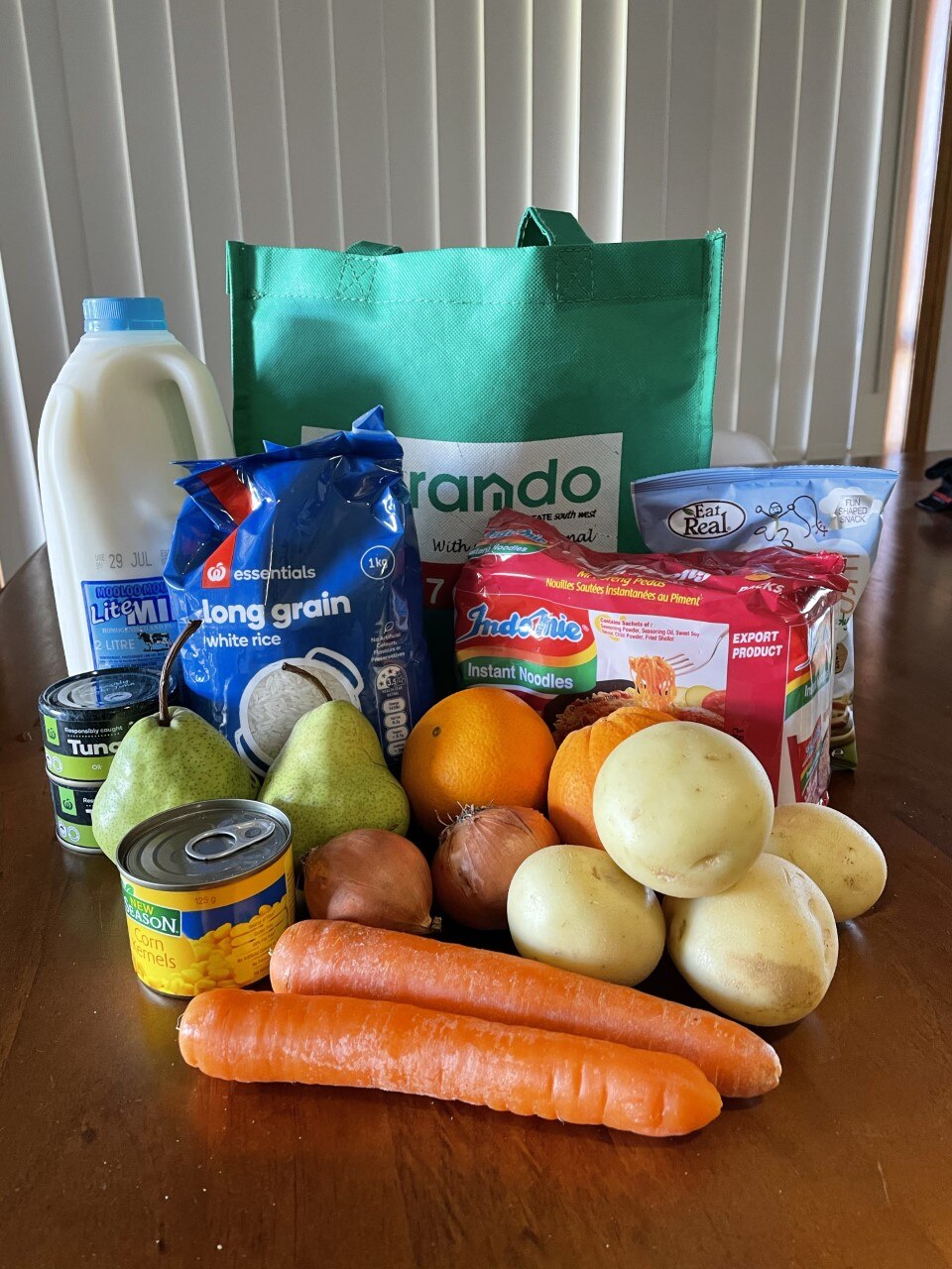 A care package, featuring fresh vegetables, milk, noodles, fruit and tuna.