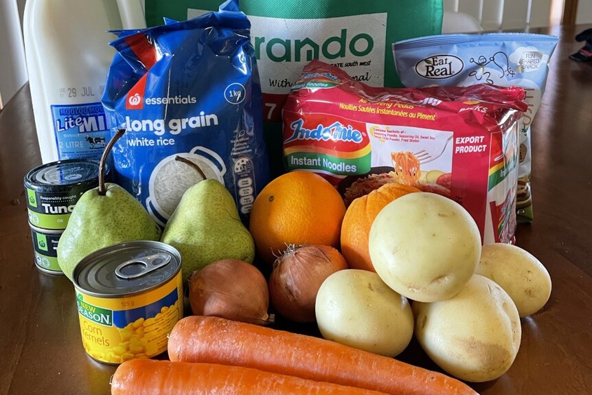 A care package, featuring fresh vegetables, milk, noodles, fruit and tuna.