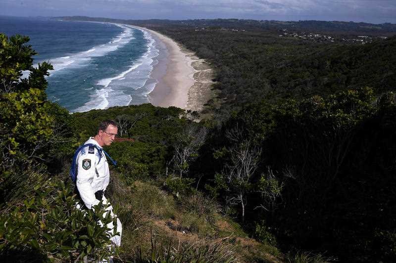 A police rescue officer beats a path through a bushy headland overlooking the ocean.