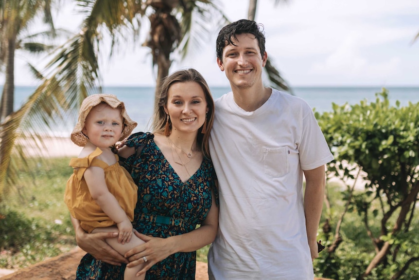 Young couple with the mother holding a toddler, standing by a beach with palm trees