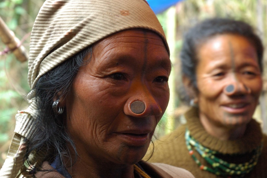 Two women look past the camera in traditional Apa Tani dress, featuring nasal stretchers