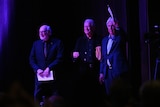 Three men in suits on a stage.
