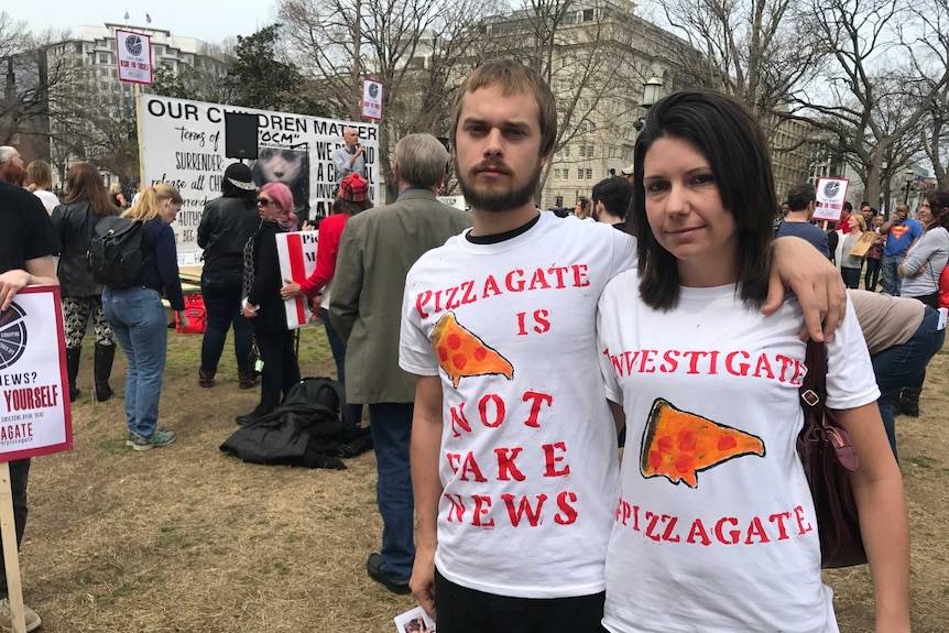 Two people at a demonstration wearing Pizzagate t-shirts.