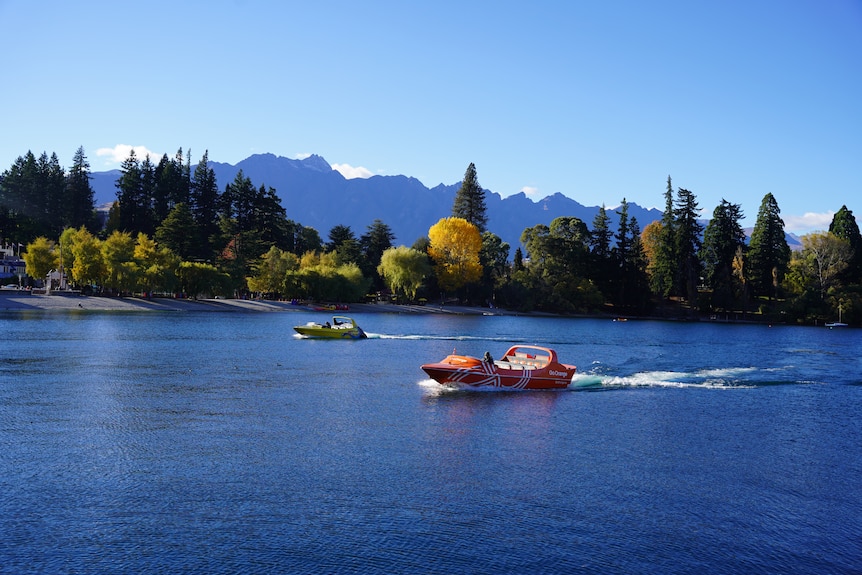 Two speed boats jet across a blue lake in New Zealand. 