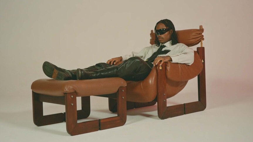 Steve Lacy wearing sunglasses and smart casual reclining in a vintage chair and lazyboy