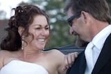 Jennie and Ray give smile deeply at each other in an open-top car. They are in wedding dress and suit.
