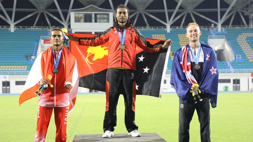 Three men stand on a podium, each holding their country's flag. PNG is on top, Tahiti second and New Zealand third.