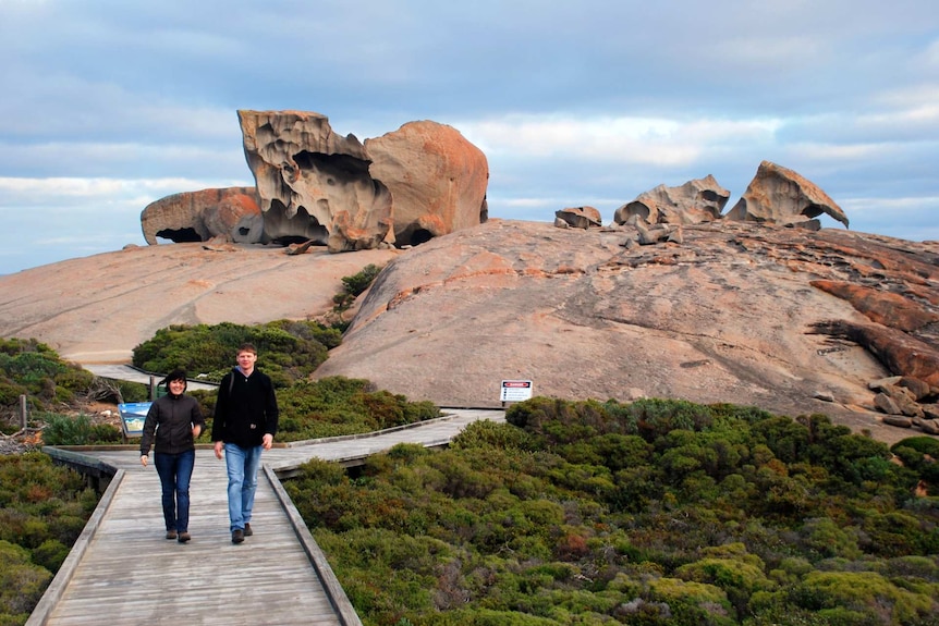 Two people walk away from a rock formation