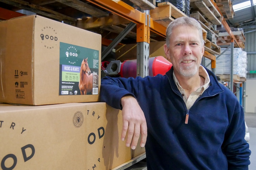 A man leans on a box with "good country hemp" labels. 