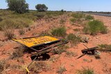 A damaged and fallen over sign beside an outback Pilbara highway