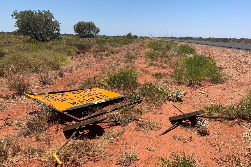 A damaged and fallen over sign beside an outback Pilbara highway