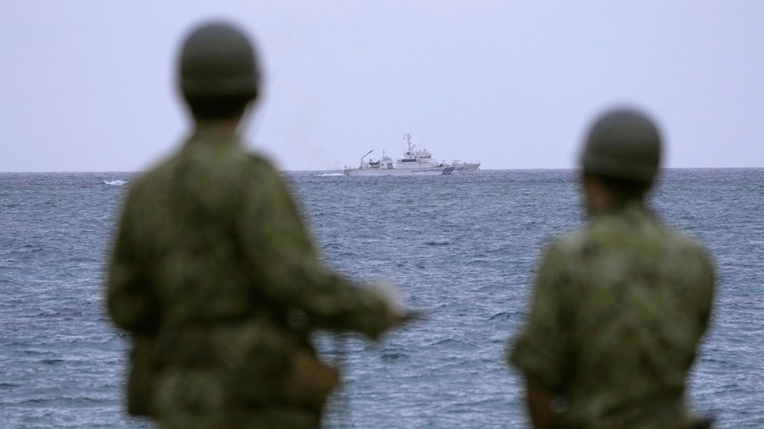 Japanese military members watch a coast guard ship searching for a missing helicopter at sea