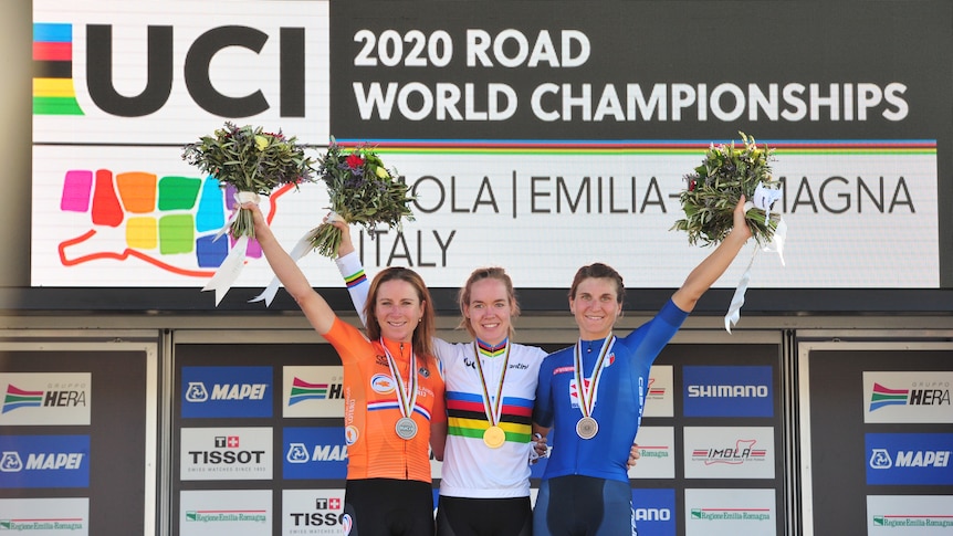 Three women standing on a podium, with medals around their necks and smiling after placing top three in cycling race 