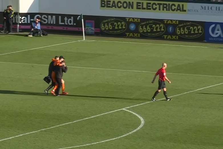 Matt Macey is carried off the field, supported by two players