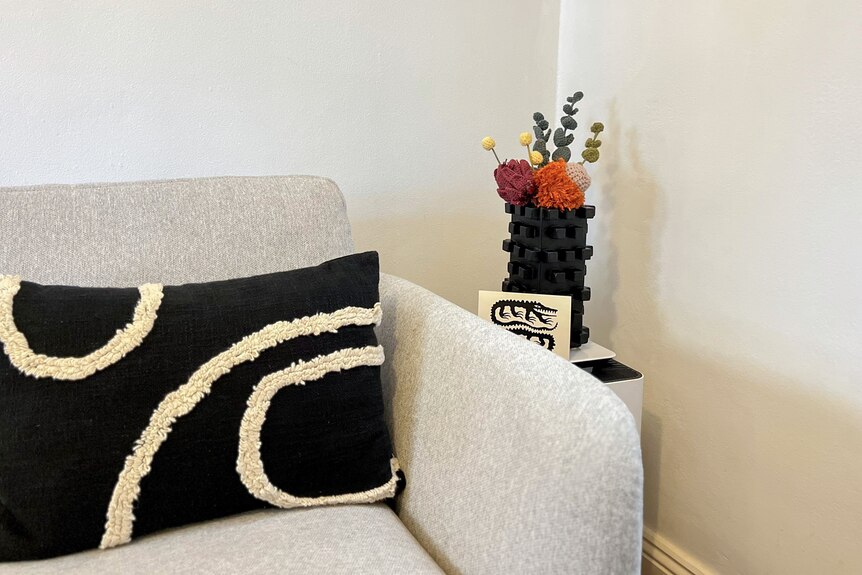 A black vase holds Candace's bouquet of crochet flowers next to a grey couch.