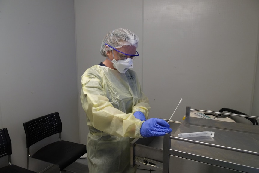 A hospital staff member in PPE with a COVID swab.