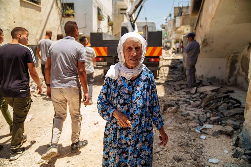 An older woman in a veil walks through rubble