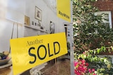 A yellow sold sticker on a real estate billboard.