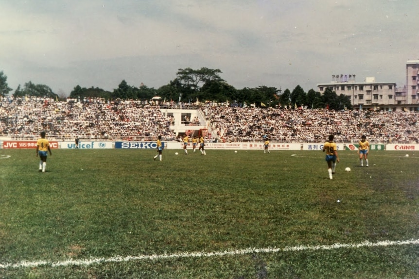 A soccer team wearing yellow, blue and white kicks balls around on a field in front of fans