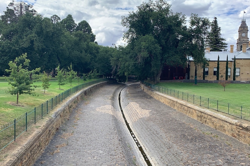 Long winding section of bluestone and concrete, a dry bendigo creek in between two patches of grass.
