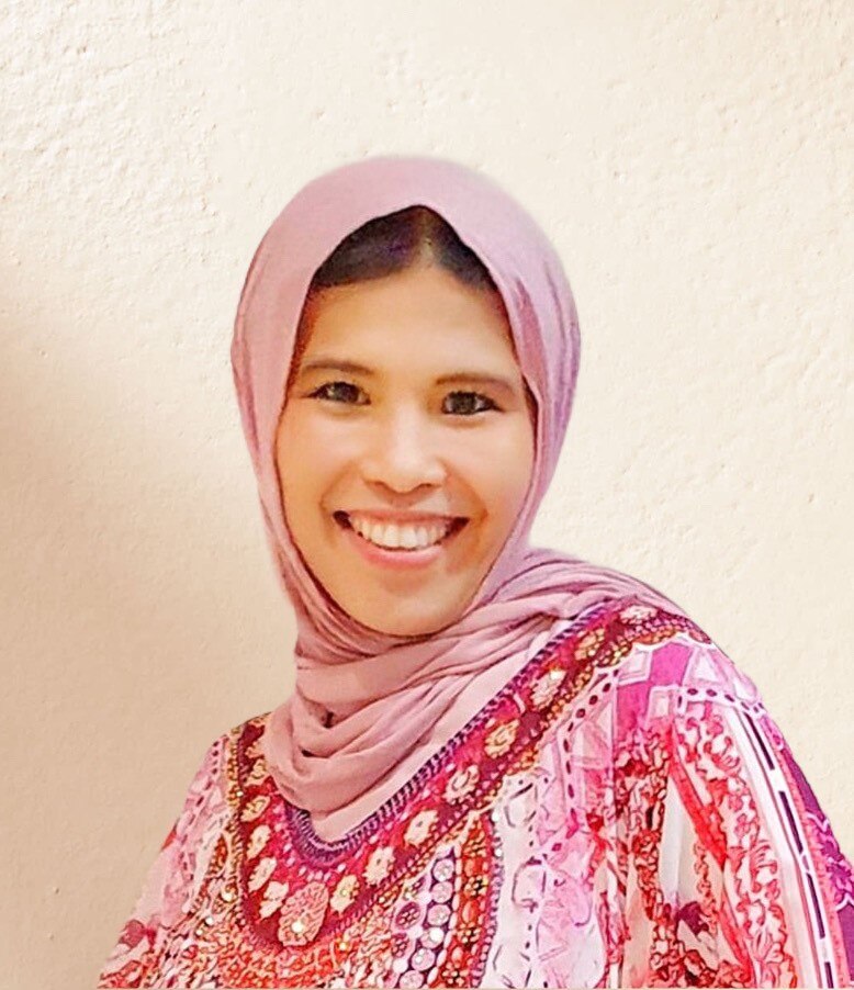 portrait of a young woman wearing a pink headscarf smiling at the camera. 