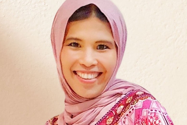 portrait of a young woman wearing a pink headscarf smiling at the camera. 