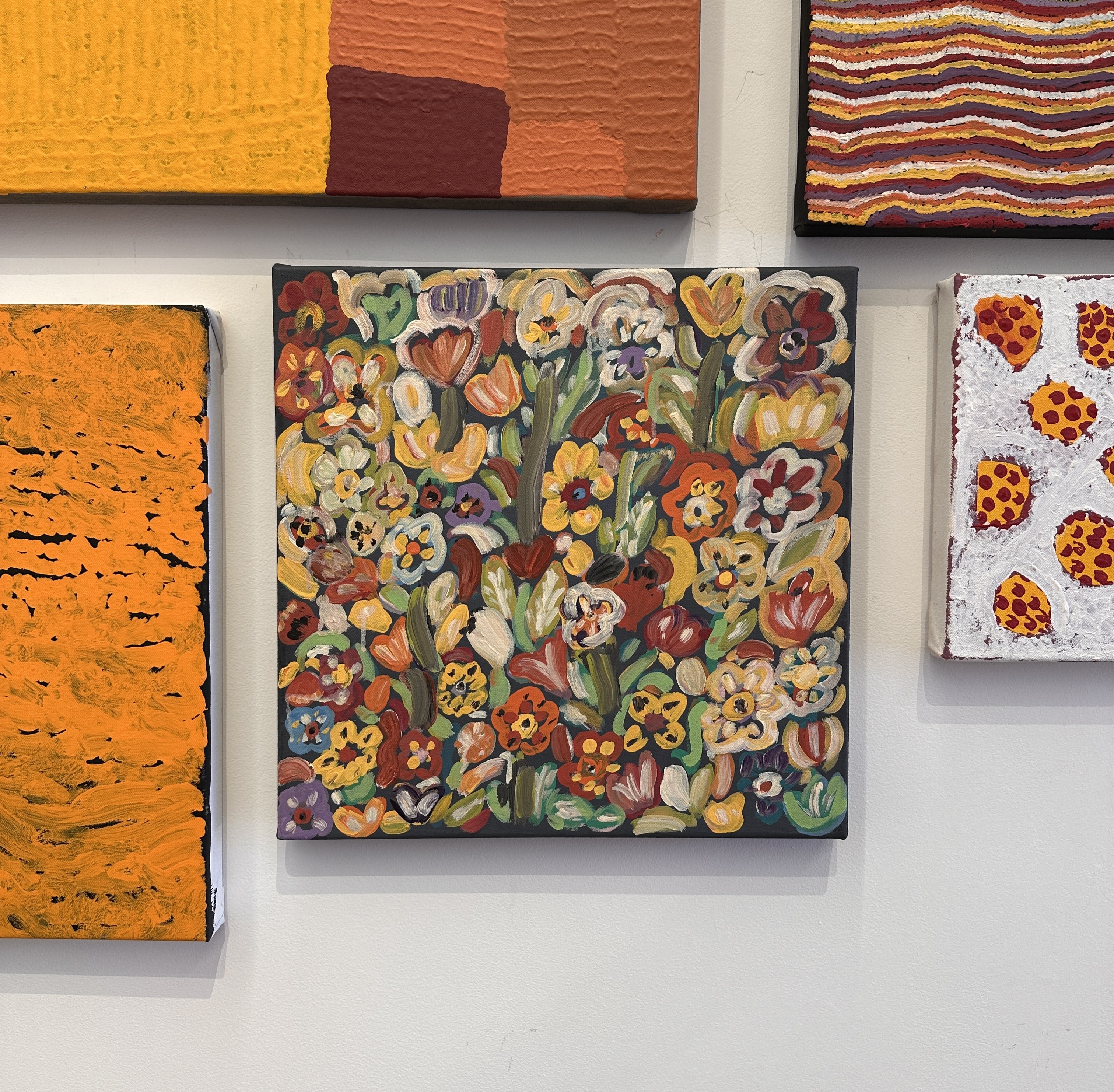 A painting of a range of colourful flowers with acrylic paint on a canvas hung on a wall.