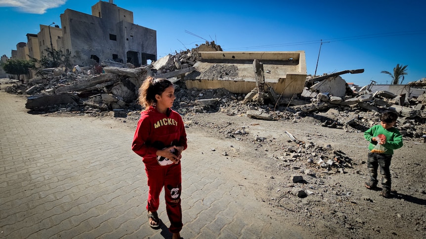 A little girl walks past rubble 