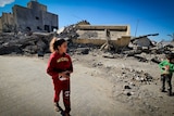 A little girl walks past rubble 
