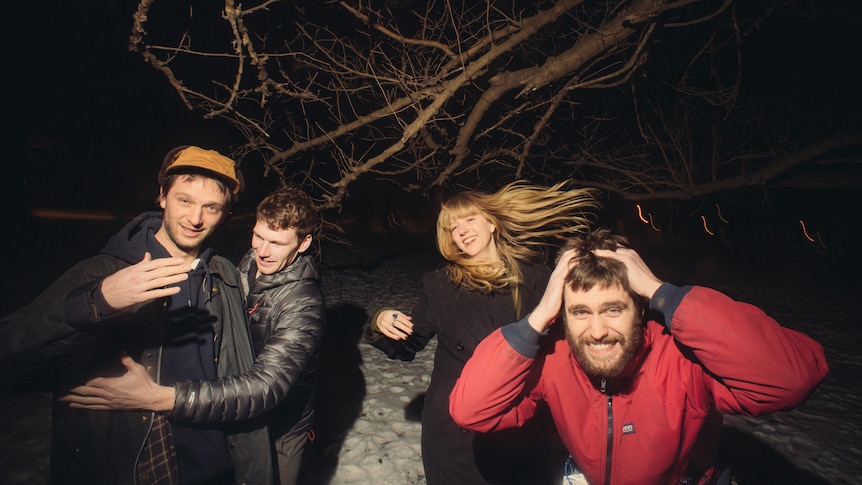 Three men and one woman smile as they gather in a snowy forest at night