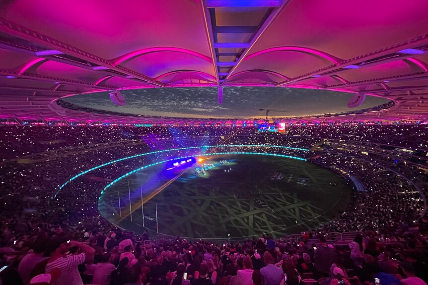 A photo of Perth Stadium under purple and pink lights. 