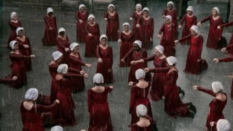 Frauen in roten Kleidern und weißen Hüten stehen im Regen im Kreis.