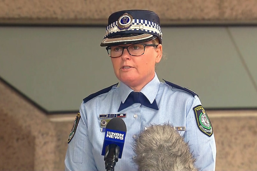 A woman with glasses wearing a police uniform talks into microphones.