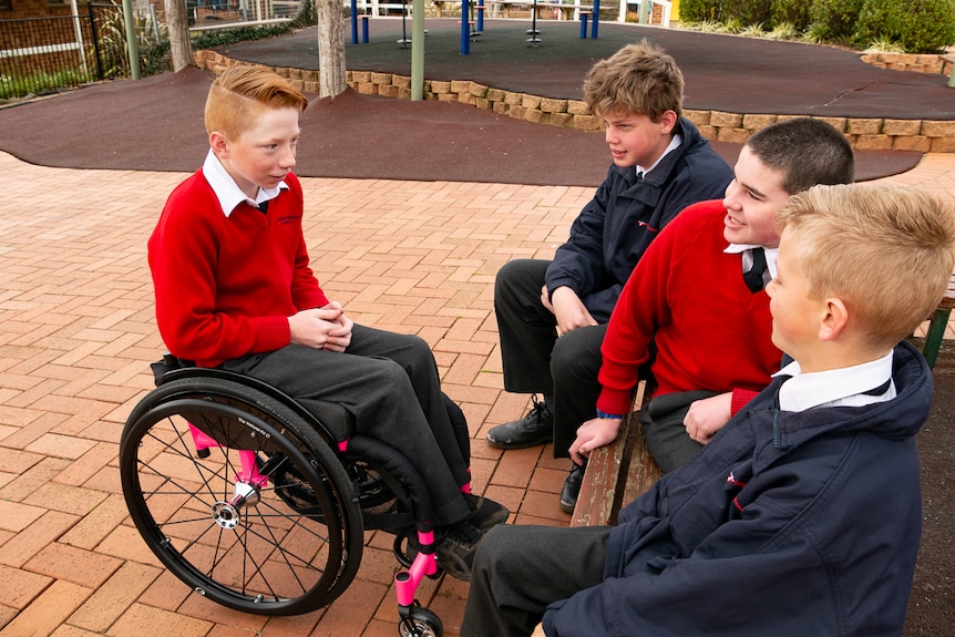 A boy in a wheelchair talking to three of his schoolmates.
