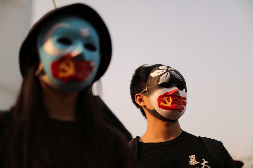One person wears an East Turkistan mask and another a Hong Kong flag mask, both with Chinese flags covering their mouths.