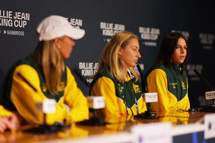 Three Australian tennis players sit in a row in their tracksuits