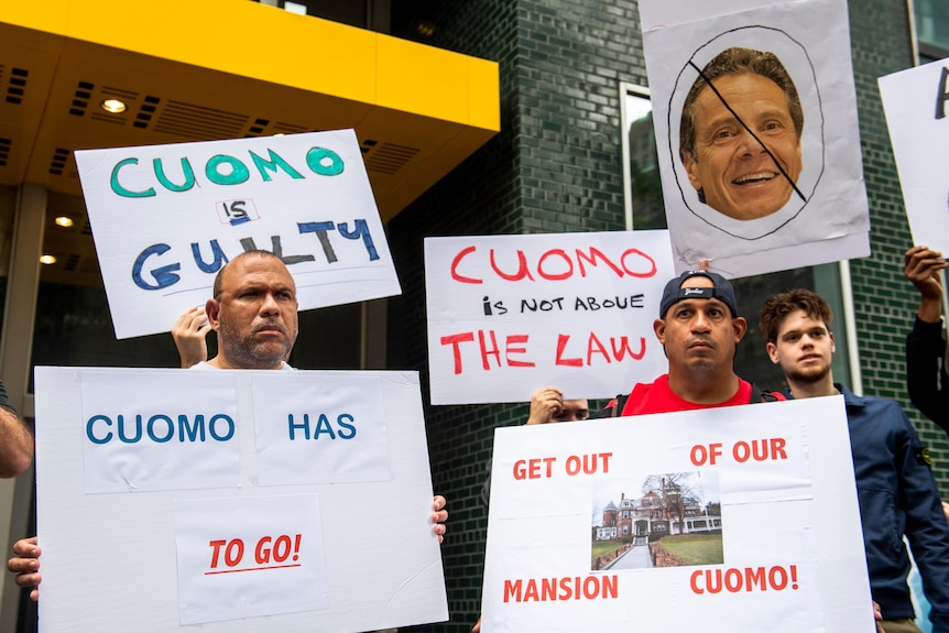 Protesters hold up signs outside the office of New York Governor Andrew Cuomo demanding he resign