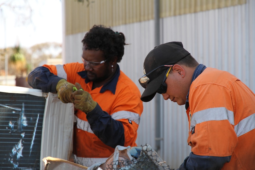 Two men in orange hi vis dismantling an air conditioner. 